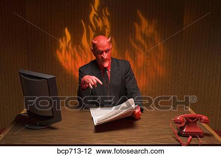 Stock Image - Businessman dressed as devil reading newspaper. Fotosearch