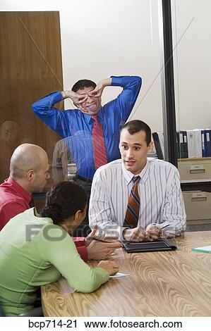 Businessman making faces through glass wall at co-workers View Large Photo Image Stock Image - Businessman making faces through glass wall at co-workers. Fotosearch