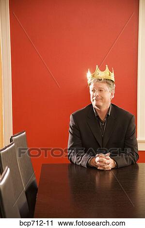 Stock Image - Businessman wearing gold crown in conference room. Fotosearch