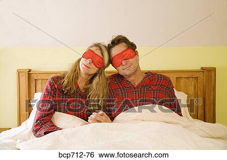 Couple sitting in bed wearing eye masks View Large Photo Image Stock Photograph - Couple sitting in bed wearing eye masks. Fotosearch