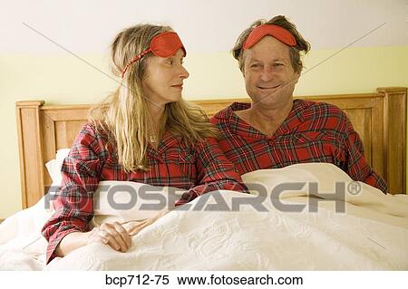 Couple sitting in bed with eye masks on head View Large Photo Image Stock Photography - Couple sitting in bed with eye masks on head. Fotosearch