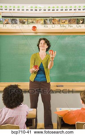 Stock Image - Female teacher juggling apples in classroom. Fotosearch