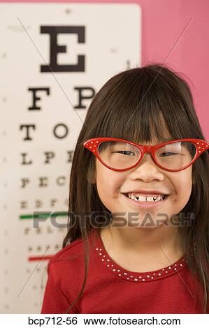 Stock Photograph - Girl wearing eyeglasses in front of eye chart. Fotosearch