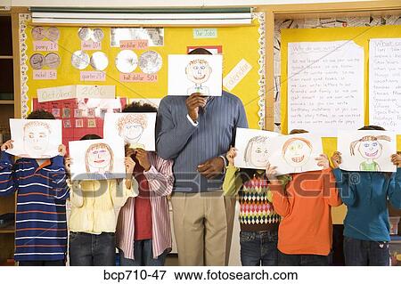 Male teacher and students holding drawings over faces View Large Photo Image Stock Photo - Male teacher and students holding drawings over faces. Fotosearch