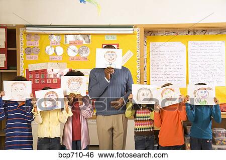 Male teacher and students holding drawings over faces View Large Photo Image Stock Photograph - Male teacher and students holding drawings over faces. Fotosearch