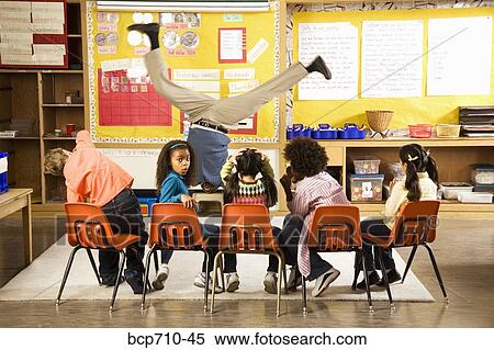 Stock Photography - Male teacher doing handstand in classroom. Fotosearch