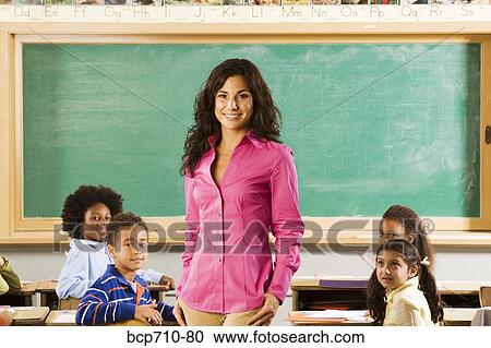 Stock Image - Portrait of female teacher and students in classroom. Fotosearch