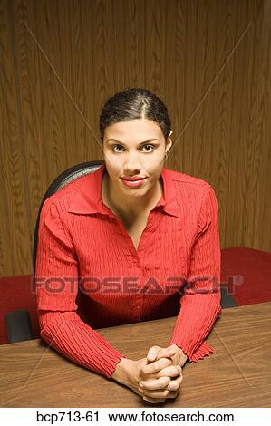 Stock Image - Portrait of woman with hands clasped at table. Fotosearch