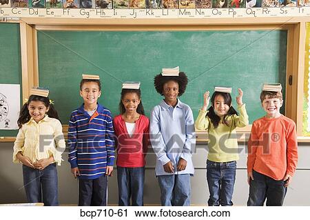 Row of students with books on their heads in classroom View Large Photo Image Stock Image - Row of students with books on their heads in classroom. Fotosearch