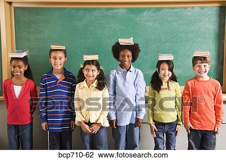 Row of students with books on their heads in classroom View Large Photo Image Stock Image - Row of students with books on their heads in classroom. Fotosearch
