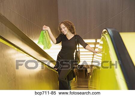 Stock Photography - Woman holding shopping bags on escalator. Fotosearch