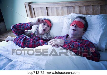 Stock Image - Woman peeking at man wearing eye mask. Fotosearch