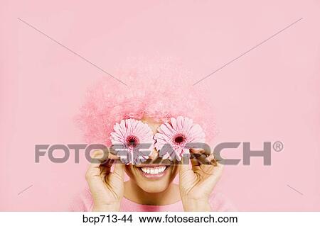 Woman wearing pink wig and holding flowers over eyes View Large Photo Image Picture - Woman wearing pink wig and holding flowers over eyes. Fotosearch