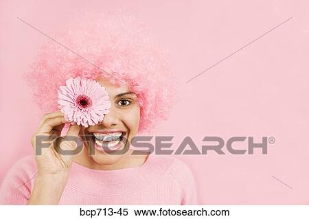 Stock Photography - Woman wearing pink wig and holding flower over eye. Fotosearch