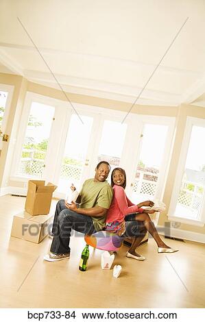 Picture - African couple eating take out in new house. Fotosearch