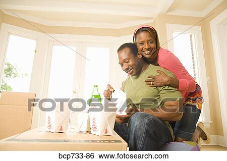 Stock Photograph - African couple eating take out in new house. Fotosearch