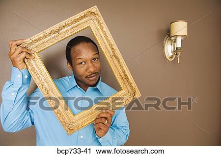 Stock Image - African man looking through picture frame. Fotosearch