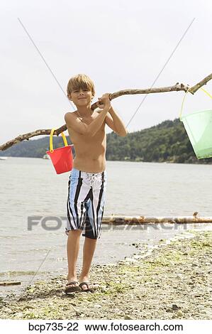 Stock Image - Boy carrying buckets at beach. Fotosearch