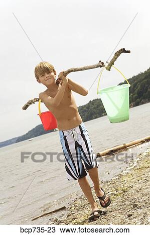 Stock Image - Boy carrying buckets at beach. Fotosearch