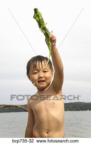 Stock Image - Boy holding stick with seaweed. Fotosearch
