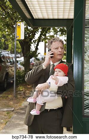 Stock Photo - Businessman holding baby at bus stop. Fotosearch