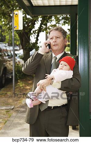 Stock Photo - Businessman holding baby at bus stop. Fotosearch