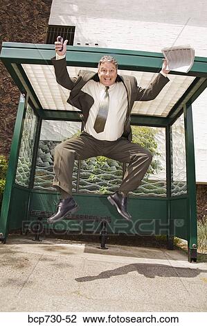 Stock Image - Businessman jumping at bus stop. Fotosearch