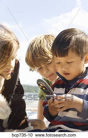 Stock Image - Children looking at cell phone. Fotosearch