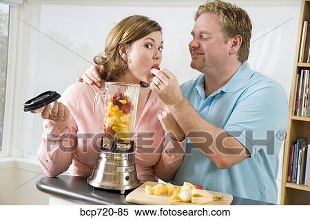 Stock Photography - Couple eating fruit while making a smoothie. Fotosearch