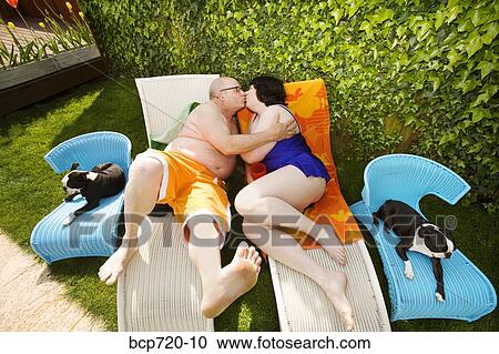 Stock Image - Couple kissing on lawn chairs in backyard. Fotosearch