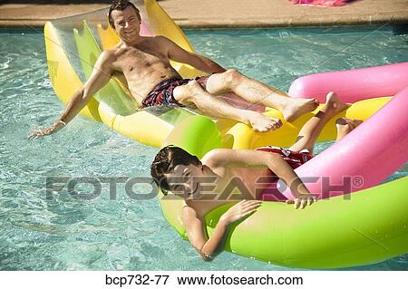 Father and son on floats in swimming pool View Large Photo Image Stock Photo - Father and son on floats in swimming pool. Fotosearch