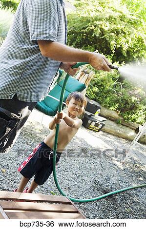 Stock Photograph - Father and son using garden hose. Fotosearch