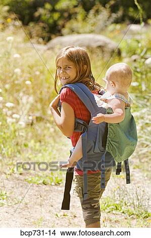 Picture - Girl carrying baby sibling on back. Fotosearch