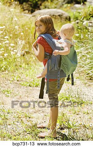 Stock Image - Girl carrying baby sibling on back. Fotosearch