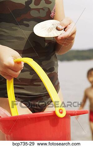 Stock Photo - Girl holding sand dollar and pail. Fotosearch
