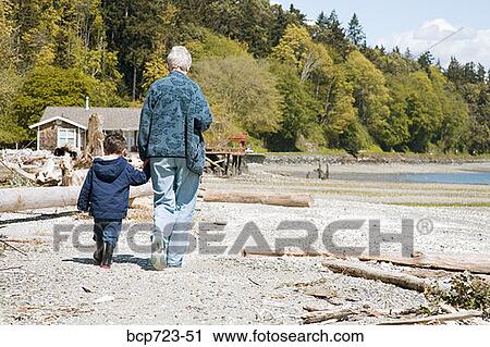 Stock Image - Grandmother and grandson walking on beach. Fotosearch