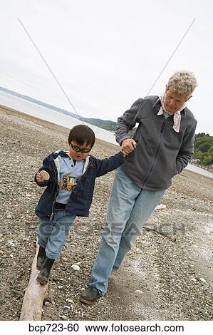Stock Image - Grandmother and grandson walking on beach. Fotosearch