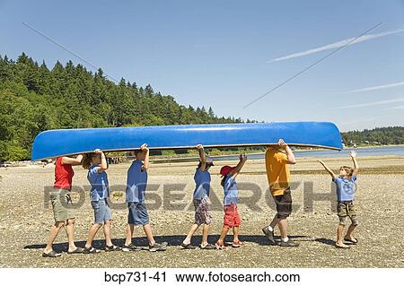 Stock Image - Male camp counselor and children carrying canoe. Fotosearch
