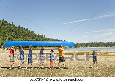 Stock Image - Male camp counselor and children carrying canoe. Fotosearch