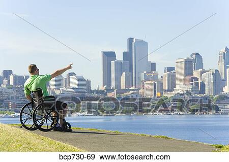 Stock Photo - Man in wheelchair pointing at city skyline. Fotosearch