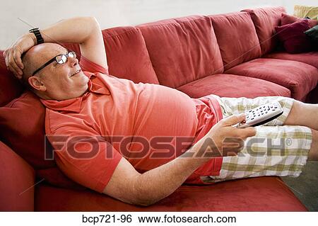 Man watching television on sofa View Large Photo Image Stock Photograph - Man watching television on sofa. Fotosearch