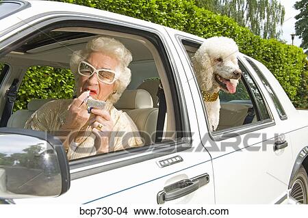 Picture - Senior woman applying lipstick in car. Fotosearch