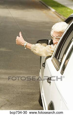 Stock Image - Senior woman giving thumbs up in car. Fotosearch
