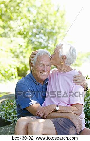 Stock Image - Senior woman kissing husband on head. Fotosearch