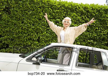 Stock Image - Senior woman standing in sunroof of car. Fotosearch