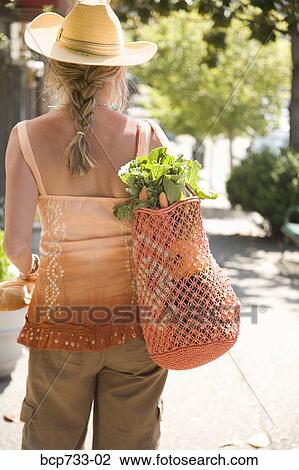 Stock Image - Woman carrying bag with vegetables. Fotosearch