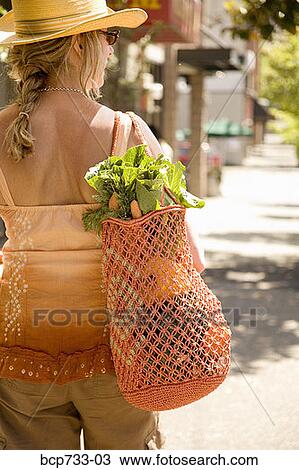 Stock Image - Woman carrying bag with vegetables. Fotosearch
