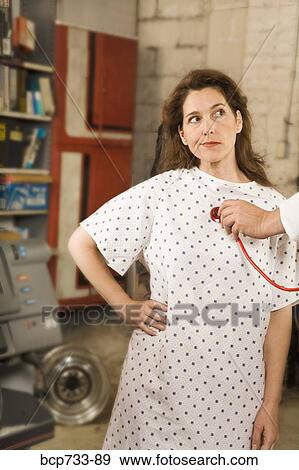 Woman in hospital gown being examined in mechanic shop View Large Photo Image Stock Photo - Woman in hospital gown being examined in mechanic shop. Fotosearch
