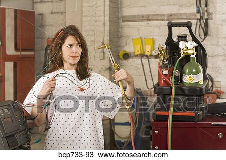 Woman in hospital gown hooked up to wire in mechanic shop View Large Photo Image Stock Image - Woman in hospital gown hooked up to wire in mechanic shop. Fotosearch