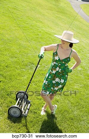 Stock Image - Woman leaning on push lawn mower. Fotosearch
